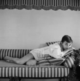 Audrey Hepburn on Striped Sofa, Rests on Book, 1954